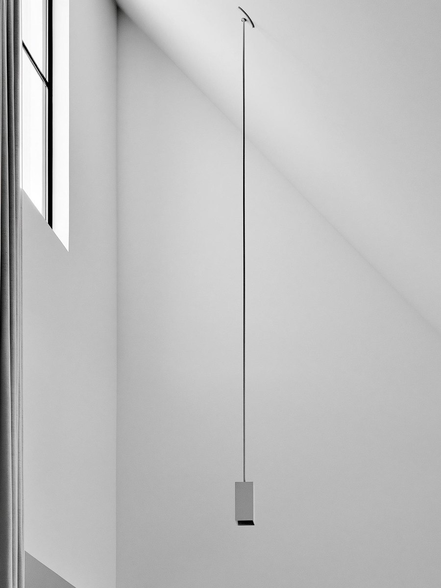 Vaulted living room ceiling seen from below and to one side, the plane of it flat and even from the ridge down to a straight line where it meets the warm off white wall, a plain fixture hanging on a long rod