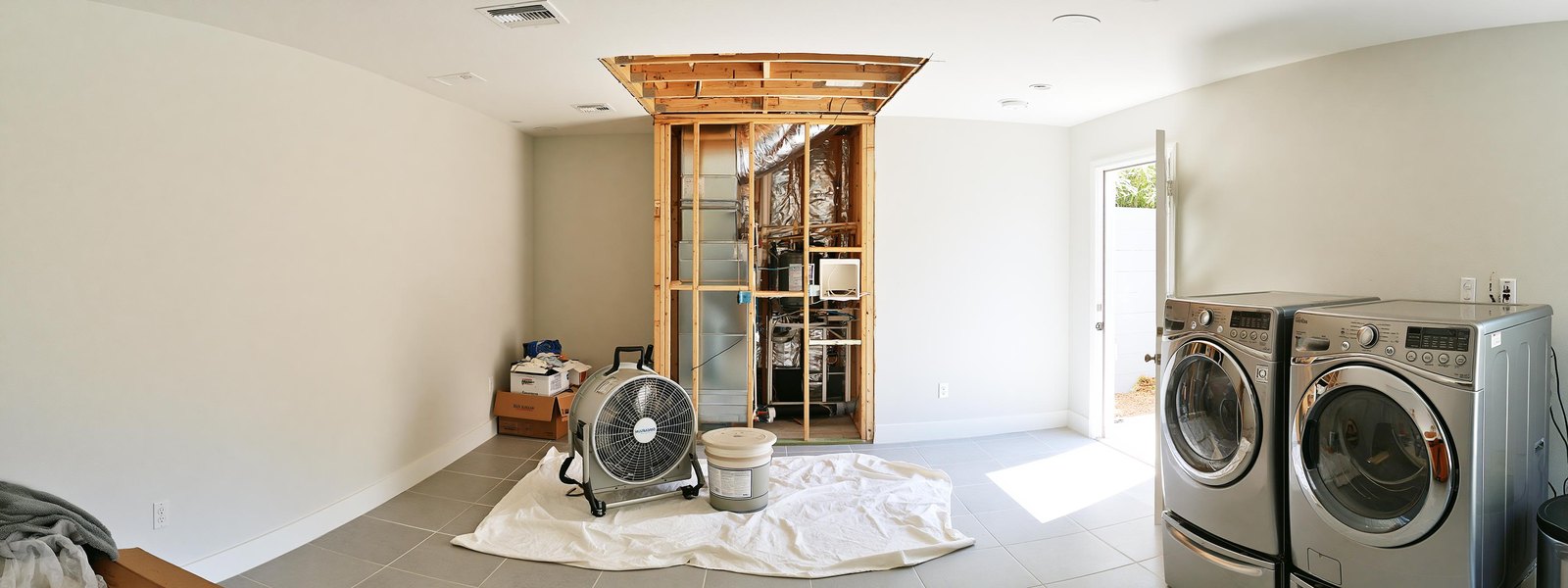 Laundry room with a neat rectangular section of ceiling opened back to the framing above, the framing clean and dry, an air mover standing on a canvas drop cloth and angled up into the opening, the rest of the ceiling flat white and even
