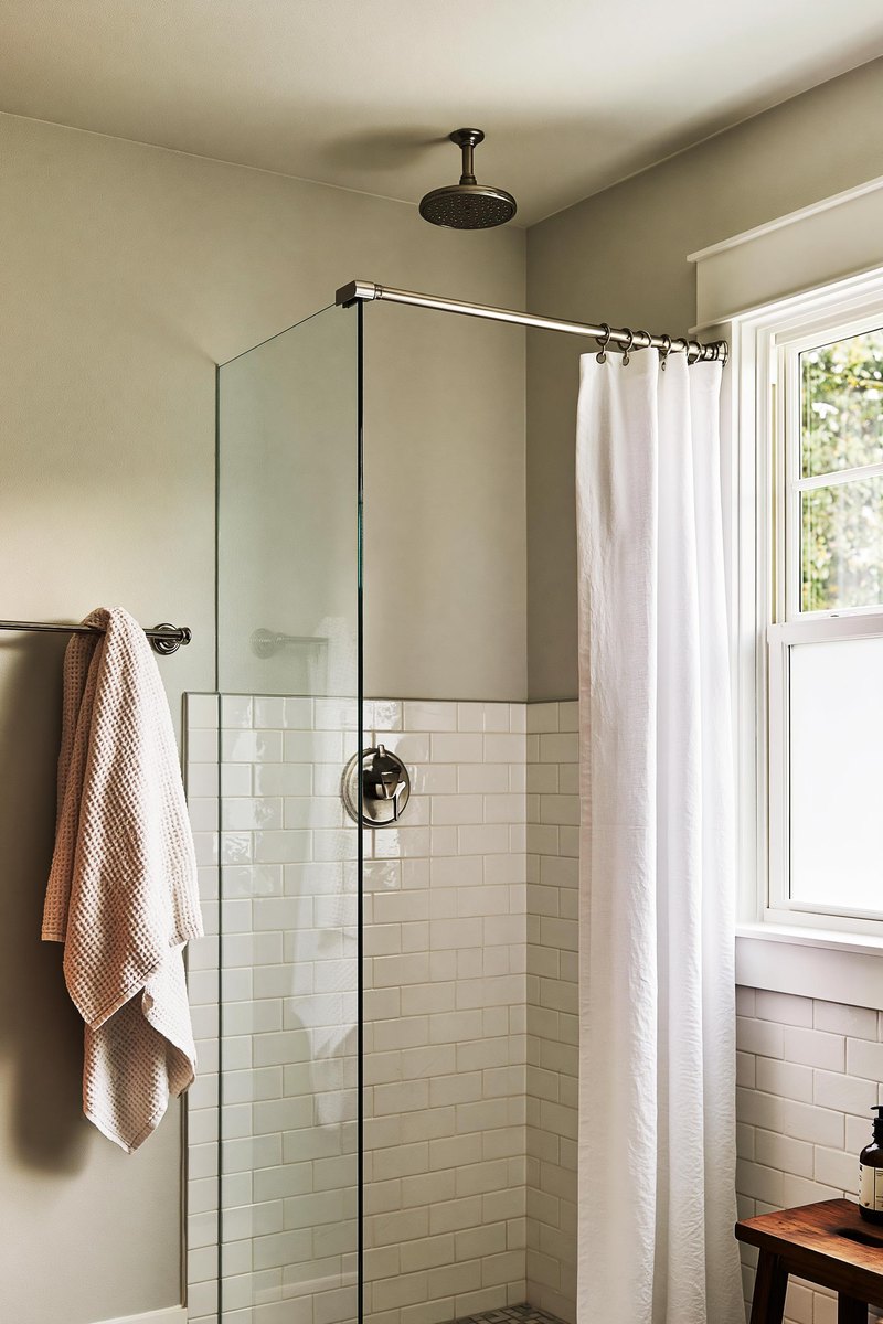 Small bathroom with a dry even flat white ceiling above the shower, soft white tile to shoulder height under a pale warm gray wall, and a folded towel on the rail